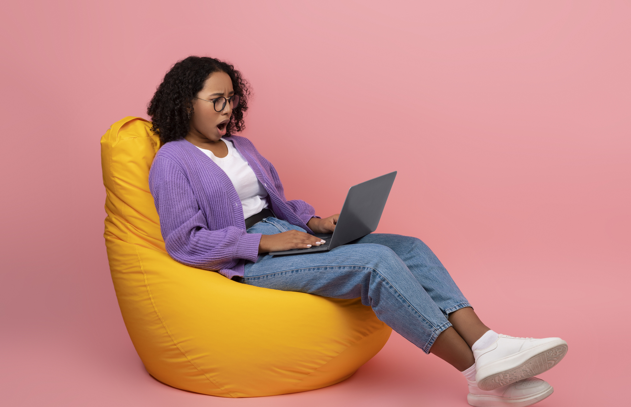 Lady sitting on a beanbag looking at the laptop with her mouth open 