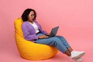 Lady sitting on a beanbag looking at the laptop with her mouth open 